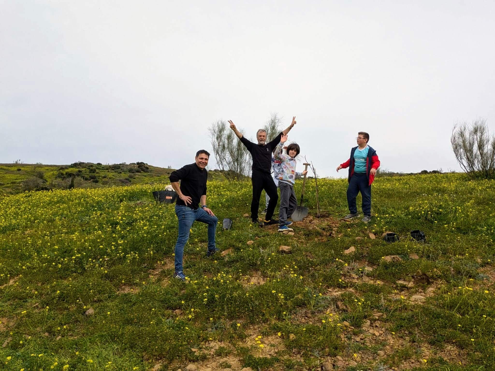Plantación en la finca de San Miguel: varias personas junto a un árbol recién plantado, entre mostaza silvestre en Álora.
